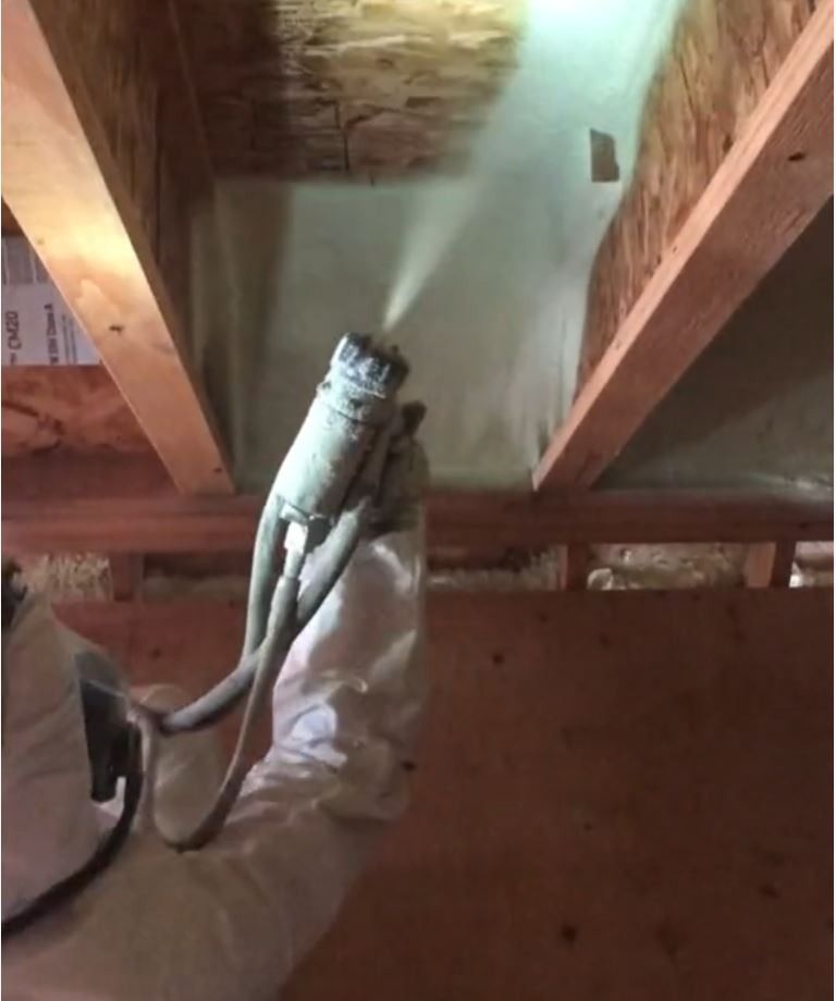 insultation worker sprays foam insulation between joists of home under construction