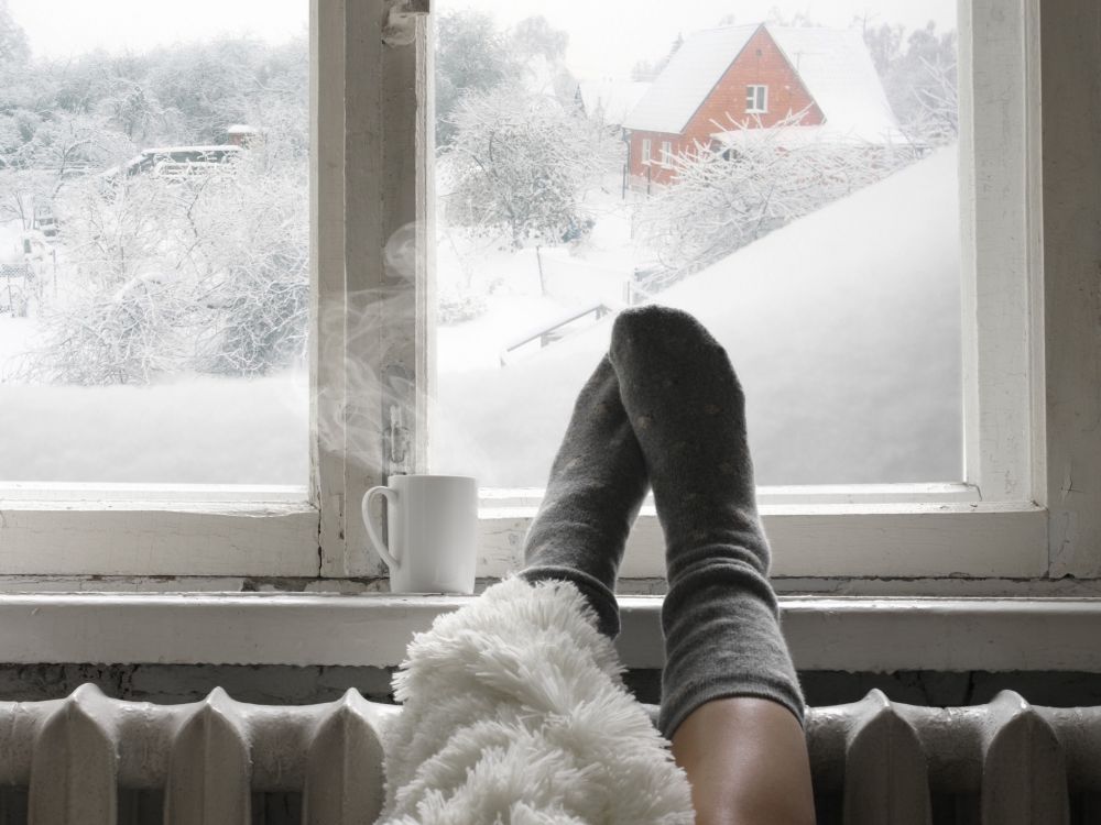 warm socked feet hanging over a sofa in front of window with winter scene