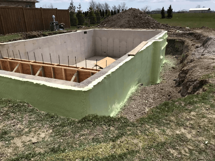 Foundation wall spray foam application Excavated concrete foundation wall coated in green spray foam insulation