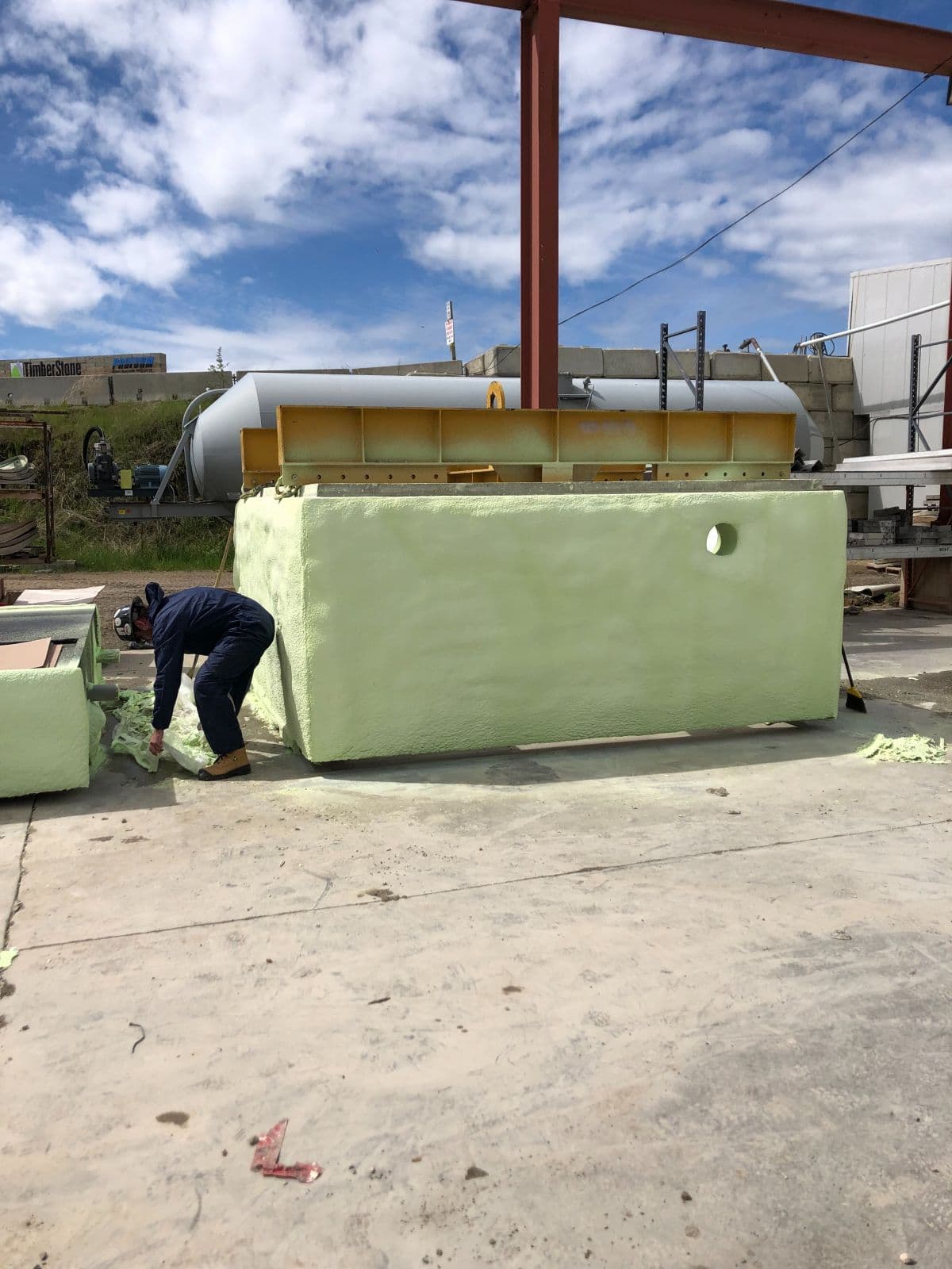 Precast concrete tank spray foam coating Worker coating a large precast concrete tank in green spray foam outdoors