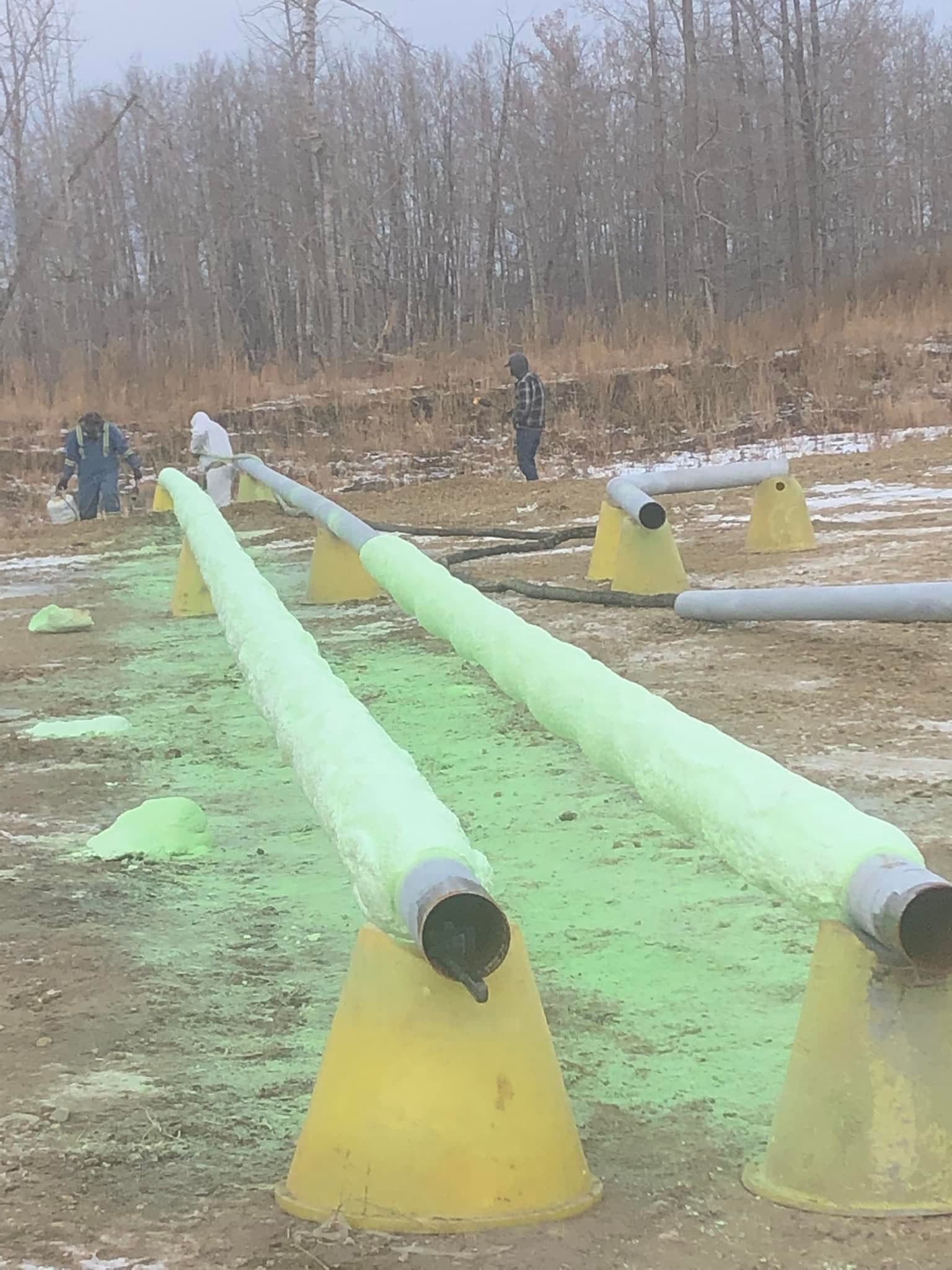 Industrial pipe insulation in the field Two workers coating large pipes with fluorescent green spray foam in a rural field