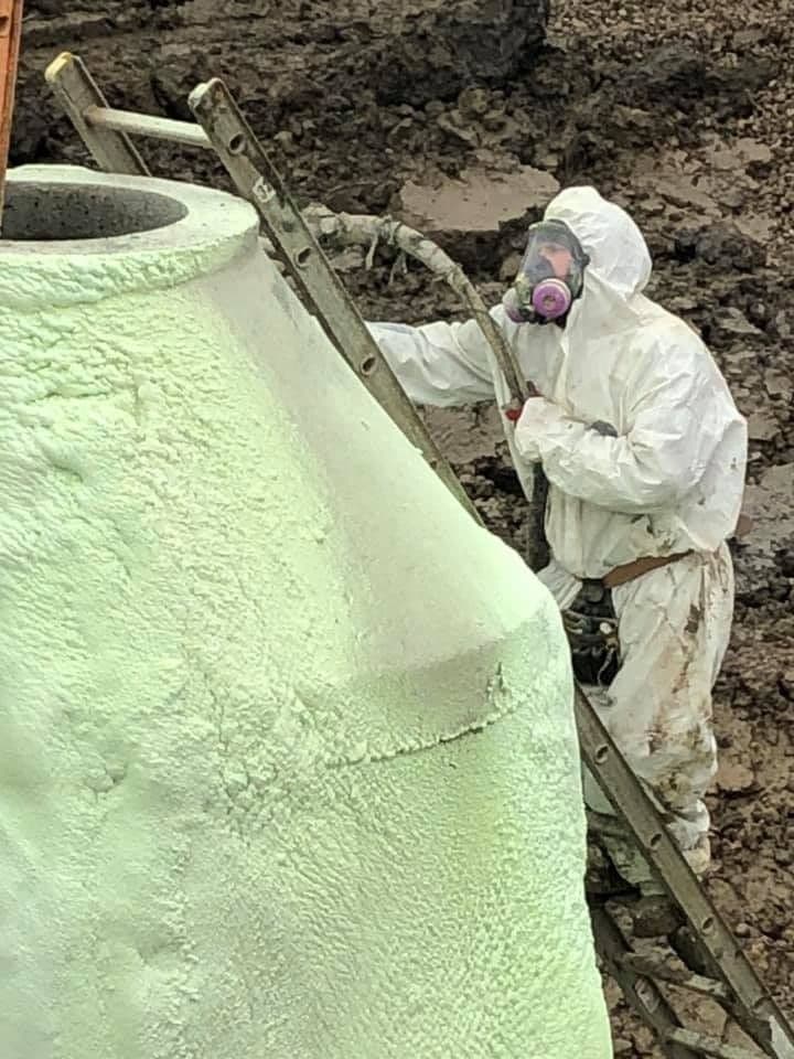 Technician spraying foam onto a concrete structure Technician in a respirator spraying green foam onto a large conical concrete structure