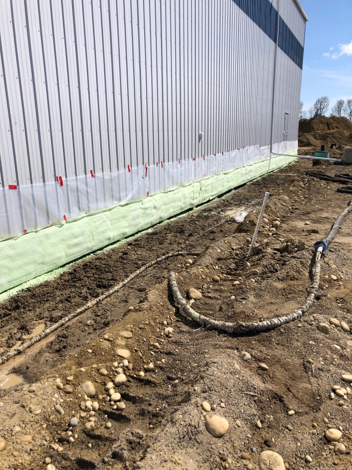 Commercial foundation spray foam application Commercial building foundation coated in green spray foam with a coiled spray hose
