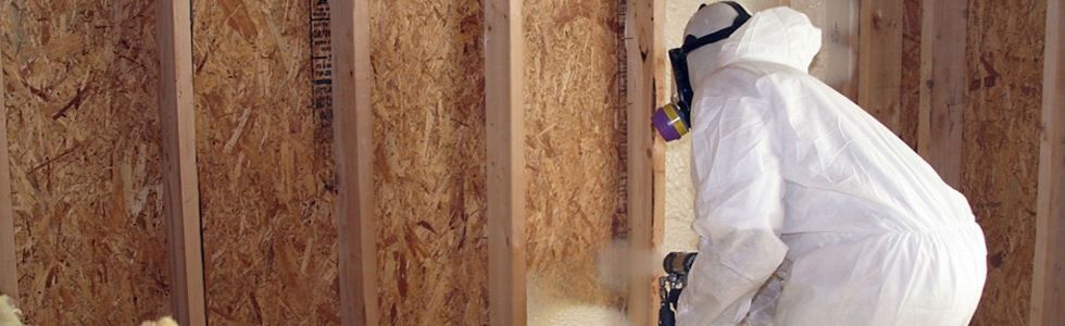 Worker with a respirator spraying green foam onto a stud wall